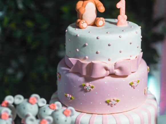 Three tier pink and white cake with a number one candle and fondant bear on top.