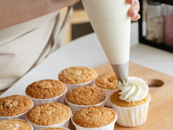 A baker piping frosting onto cupcakes.