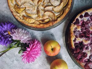 Looking down at apple and berry pies with flowers on a table.
