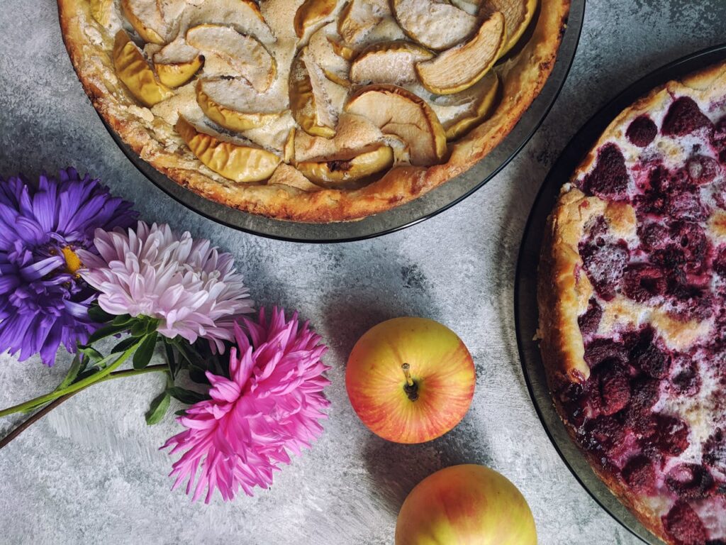 Looking down at apple and berry pies with flowers on a table.