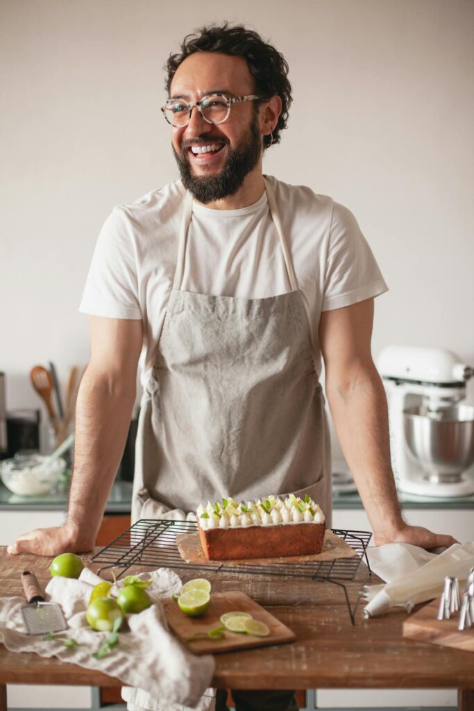 Man wearing apron stands behind a counter with a lime pound cake on it and cut lines artfully arranged.