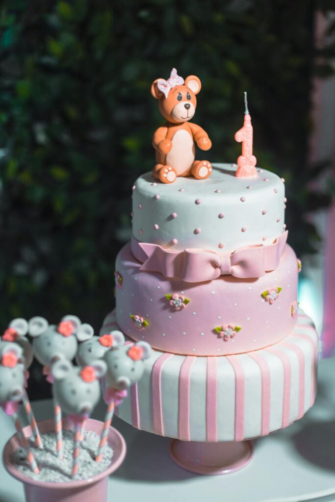 Three tier pink and white cake with a number one candle and fondant bear on top.