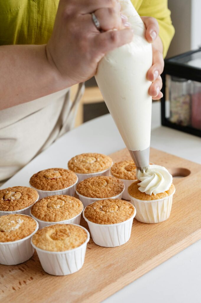A baker piping frosting onto cupcakes.