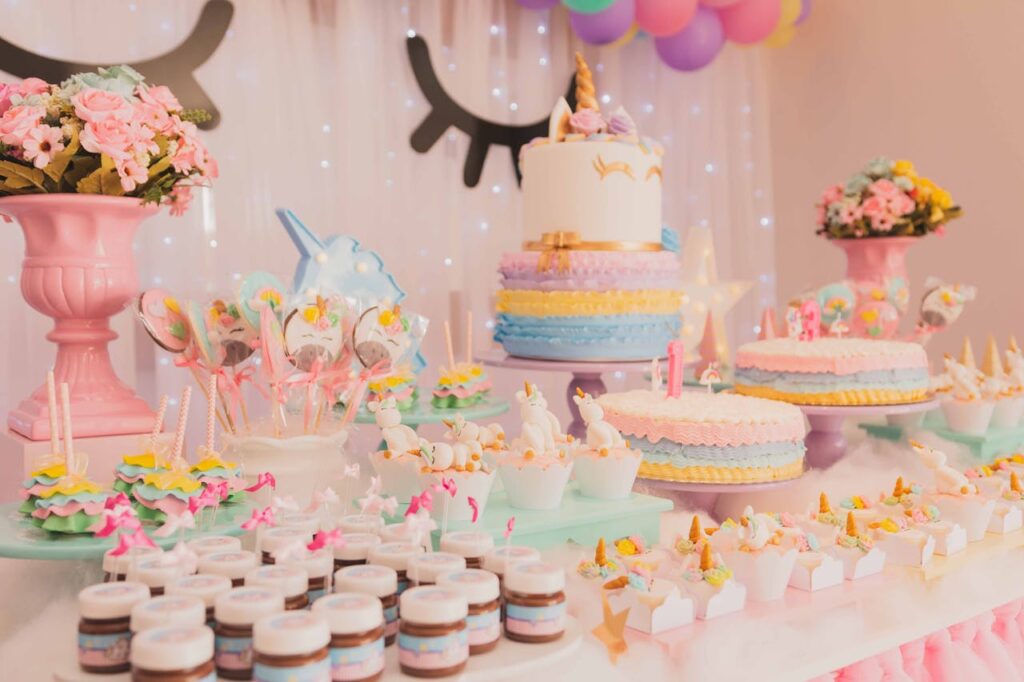 An fun dessert table featuring a variety of pastel-colored cakes, cupcakes, and sweet treats arranged on cake stands and trays, decorated with unicorn accents for a festive celebration.
