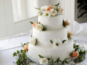 Three tier wedding cake with simple frosting and white and peach roses.