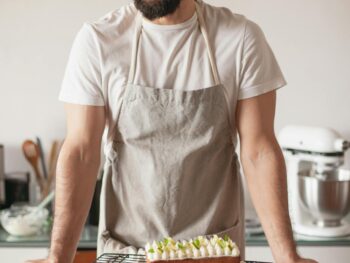 Man wearing apron stands behind a counter with a lime pound cake on it and cut lines artfully arranged.