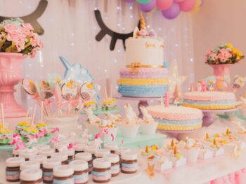 An fun dessert table featuring a variety of pastel-colored cakes, cupcakes, and sweet treats arranged on cake stands and trays, decorated with unicorn accents for a festive celebration.