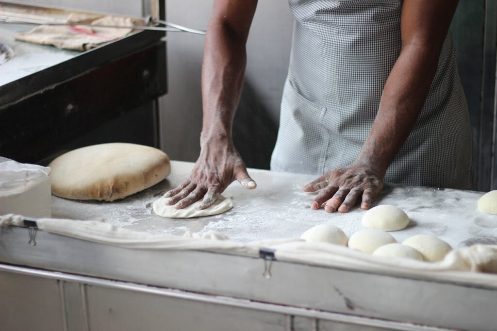 Hands of a black man kneading dough on a bakery workstation.