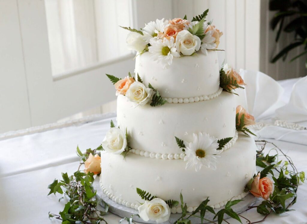 Three tier wedding cake with simple frosting and white and peach roses.