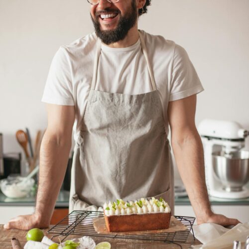 Man wearing apron stands behind a counter with a lime pound cake on it and cut lines artfully arranged.