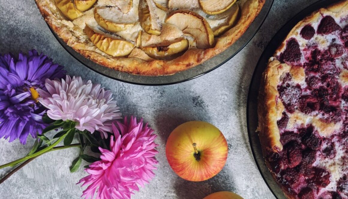 Looking down at apple and berry pies with flowers on a table.
