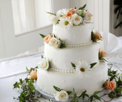 Three tier wedding cake with simple frosting and white and peach roses.