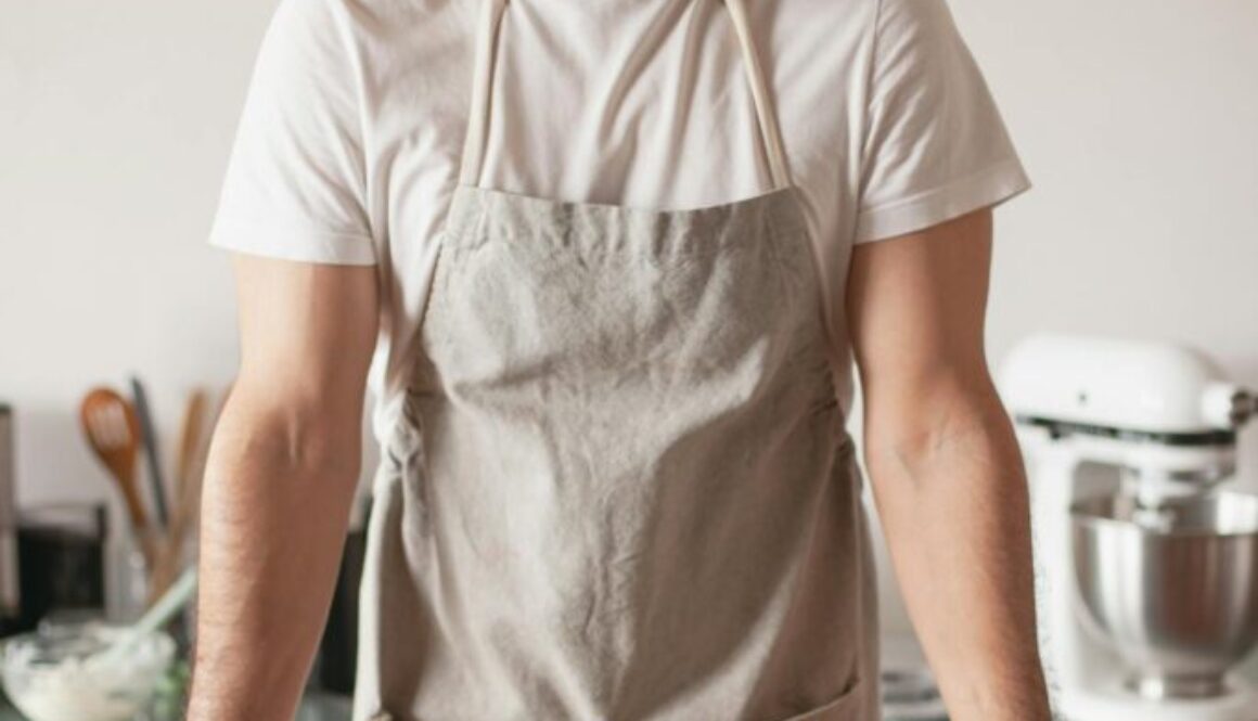 Man wearing apron stands behind a counter with a lime pound cake on it and cut lines artfully arranged.