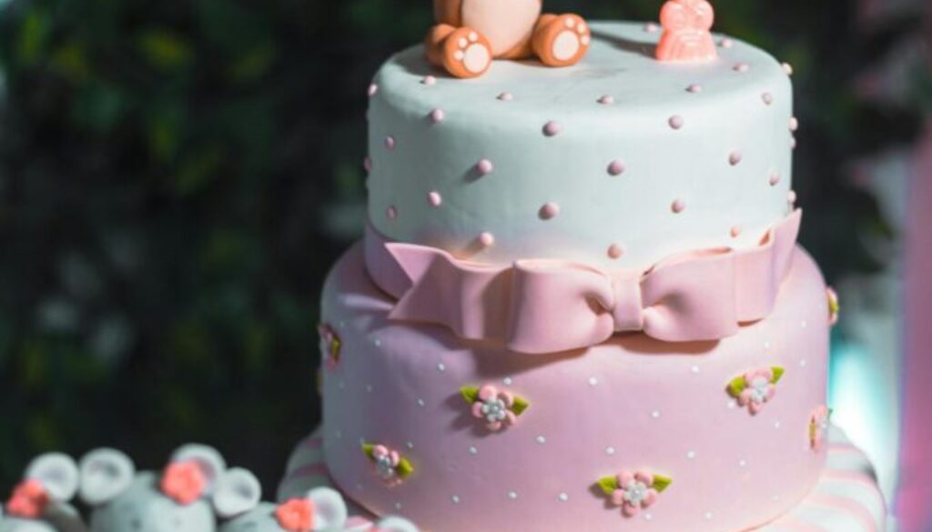 Three tier pink and white cake with a number one candle and fondant bear on top.