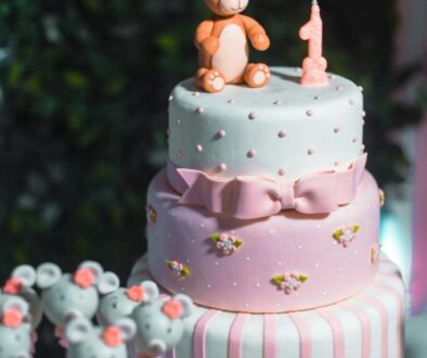 Three tier pink and white cake with a number one candle and fondant bear on top.