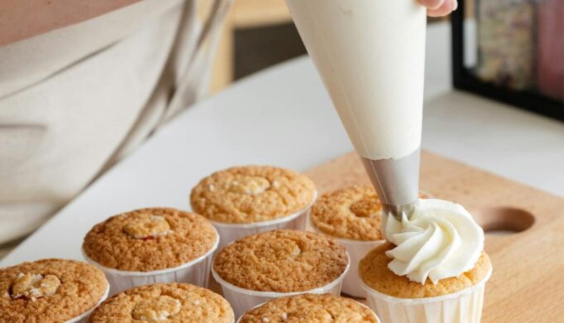 A baker piping frosting onto cupcakes.