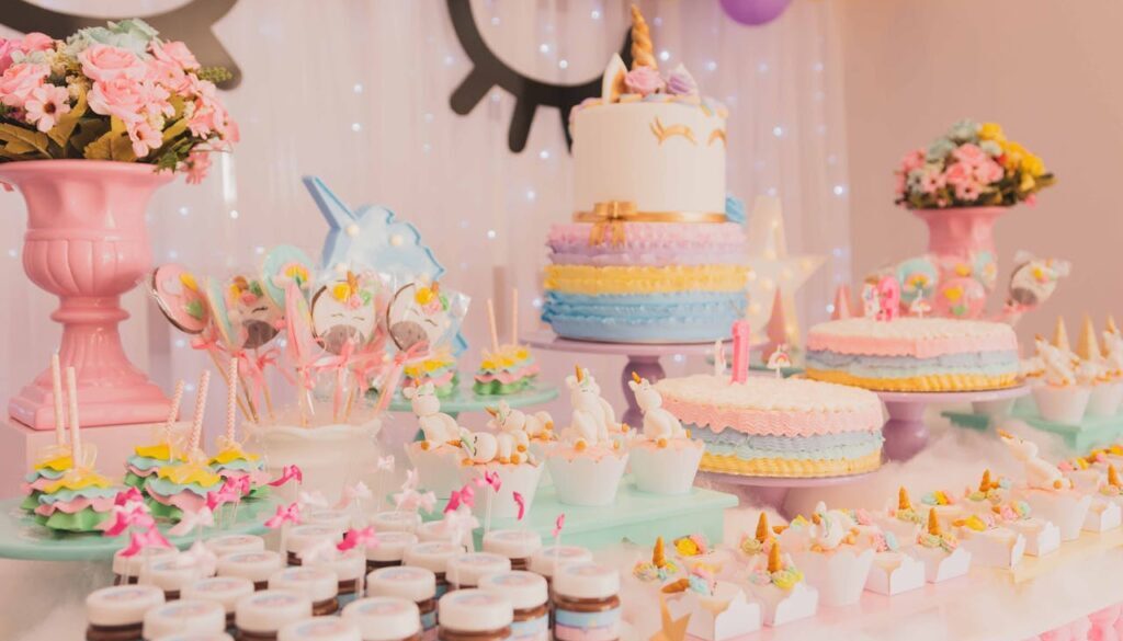 An fun dessert table featuring a variety of pastel-colored cakes, cupcakes, and sweet treats arranged on cake stands and trays, decorated with unicorn accents for a festive celebration.